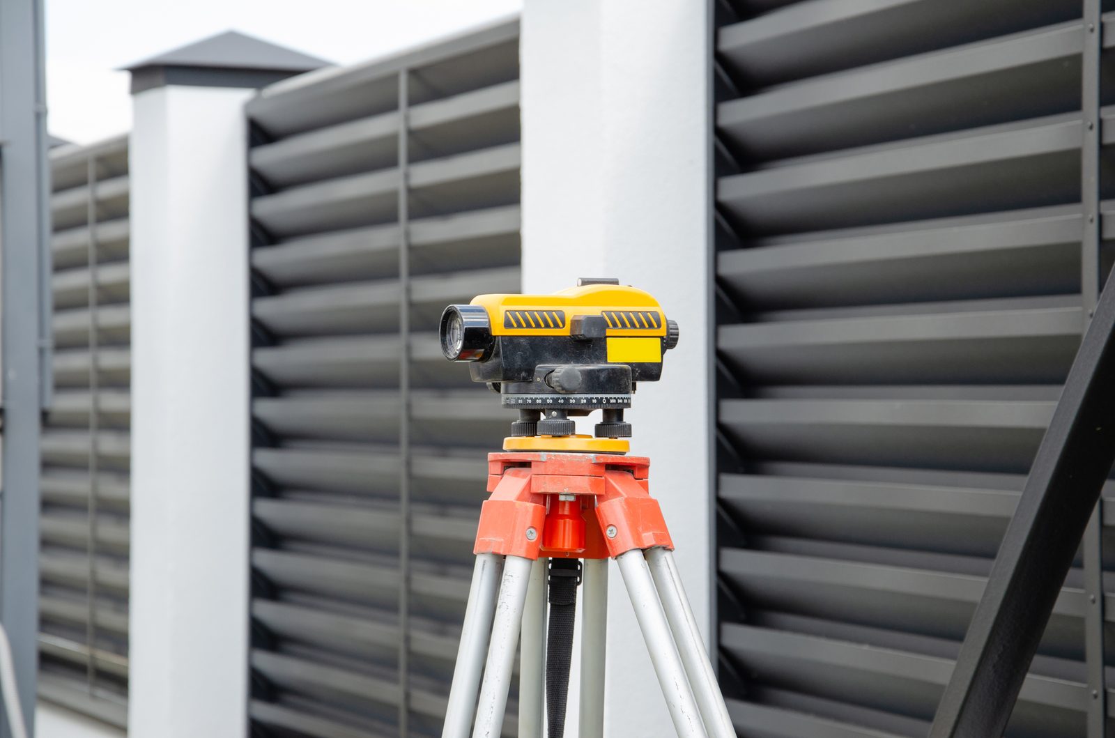 A surveying instrument on a tripod beside a modern building